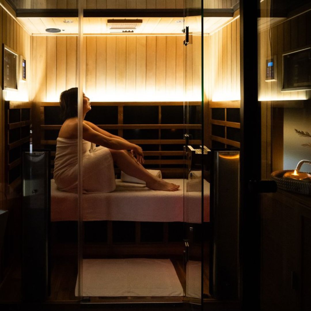 Person sitting in a sauna with wooden walls and a glass door. City Cave West Melbourne